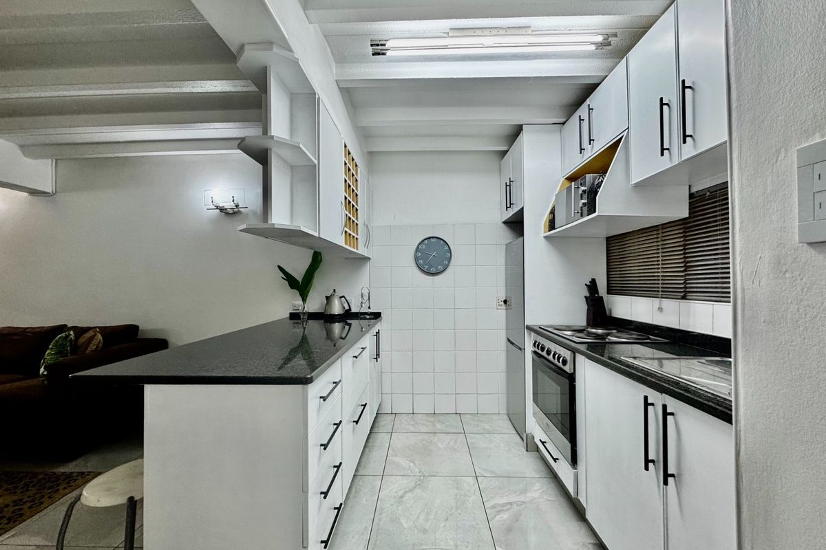 A modern galley-style kitchen featuring white cabinetry, dark granite countertops, a built-in oven with hob, and tiled flooring with an open-plan layout.