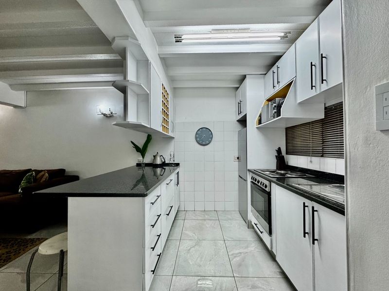 A modern galley-style kitchen featuring white cabinetry, dark granite countertops, a built-in oven with hob, and tiled flooring with an open-plan layout.