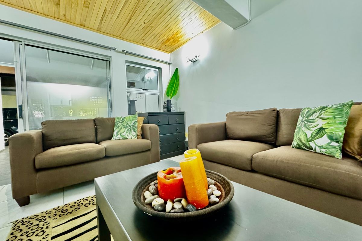 A living room featuring a vaulted timber-clad ceiling, tiled flooring, and large sliding glass doors providing natural light and access to the exterior.