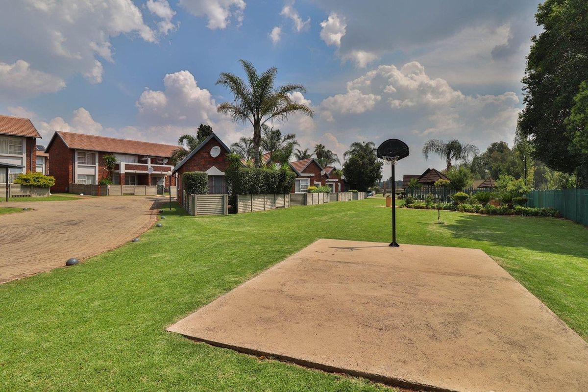 A view of the communal grounds within the townhouse complex, featuring a paved driveway, landscaped lawn, and a basketball hoop area.