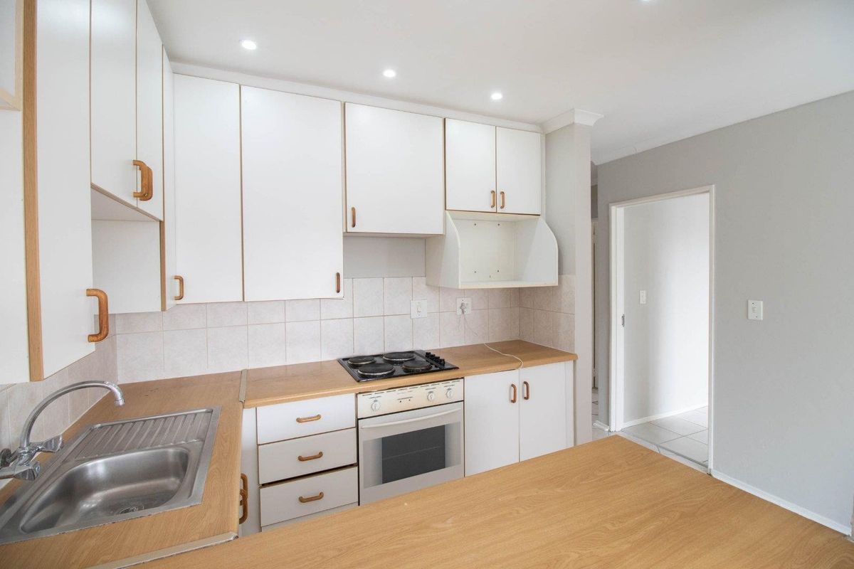 A functional kitchen featuring white cabinetry, wood-look laminate countertops, a built-in oven with hob, and a stainless steel sink.
