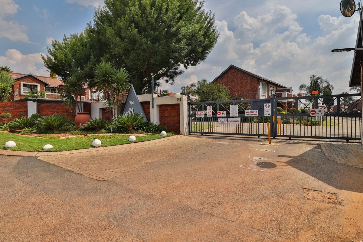 Secure gated entrance to the townhouse complex featuring brick boundary walls, paved driveway, and established landscaping.