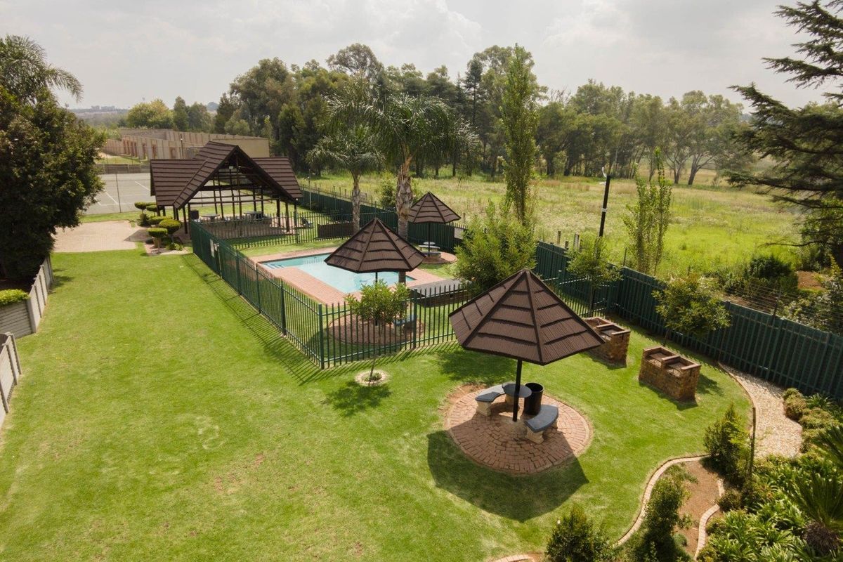 Aerial view of a communal garden area featuring a swimming pool, covered gazebo, brick braai stands, and landscaped lawn within a secure estate.