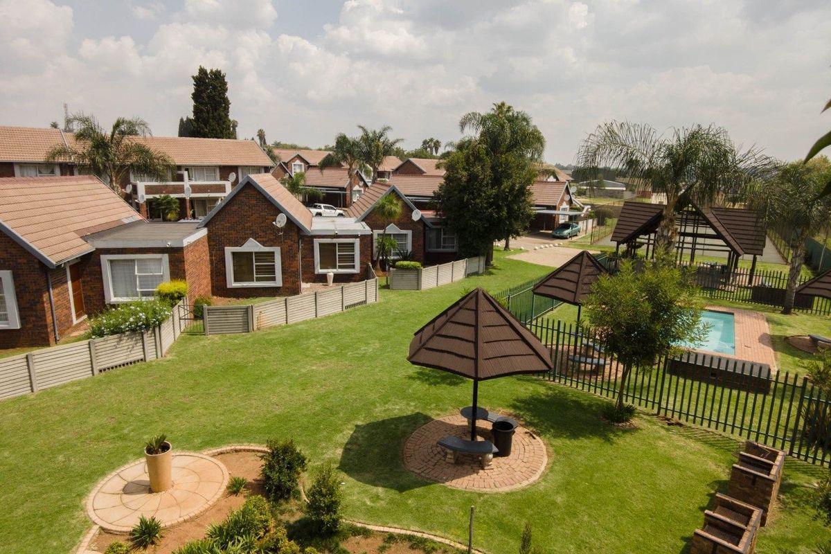 Aerial view of a townhouse complex featuring communal garden areas, a swimming pool, and brick-faced residential units with tiled roofs.