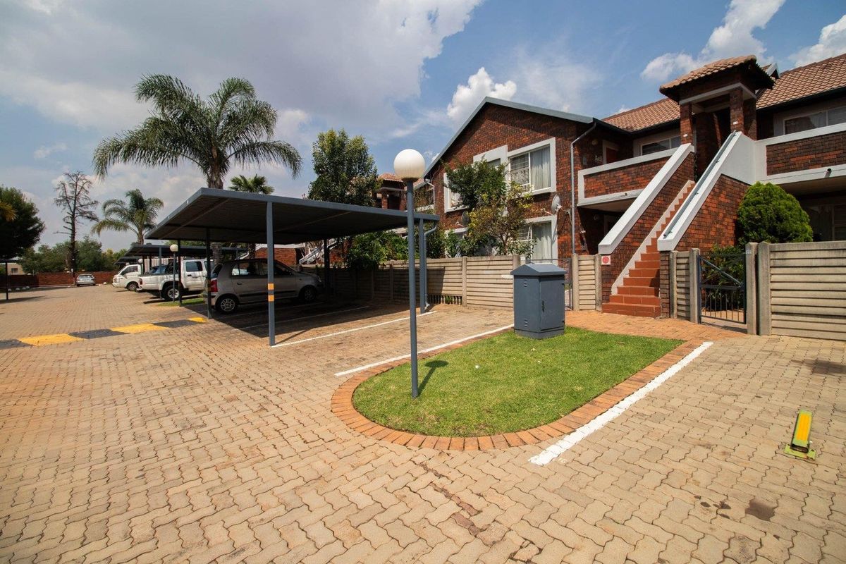 Exterior view of the townhouse complex featuring brick facade, covered parking bays, paved driveway, and external staircase access to upper units.