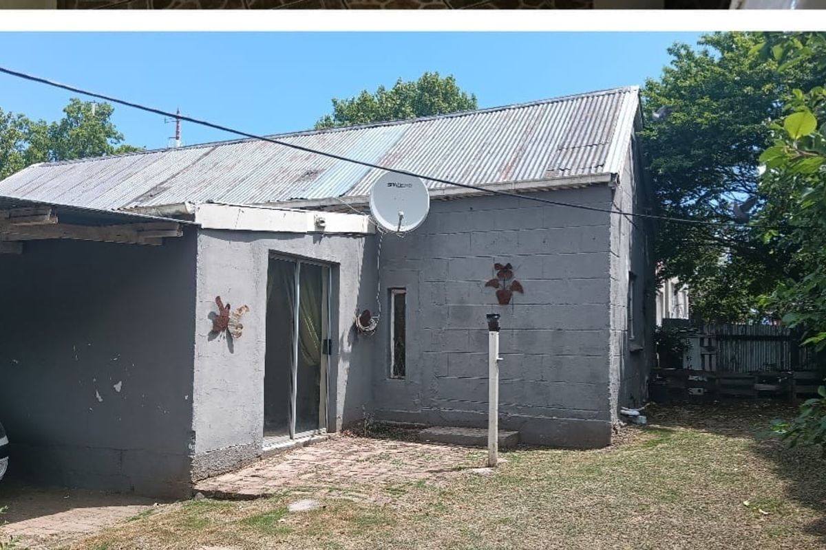 Rear view of a single-story house featuring a corrugated metal roof, concrete block walls, a sliding glass door, and an attached carport.