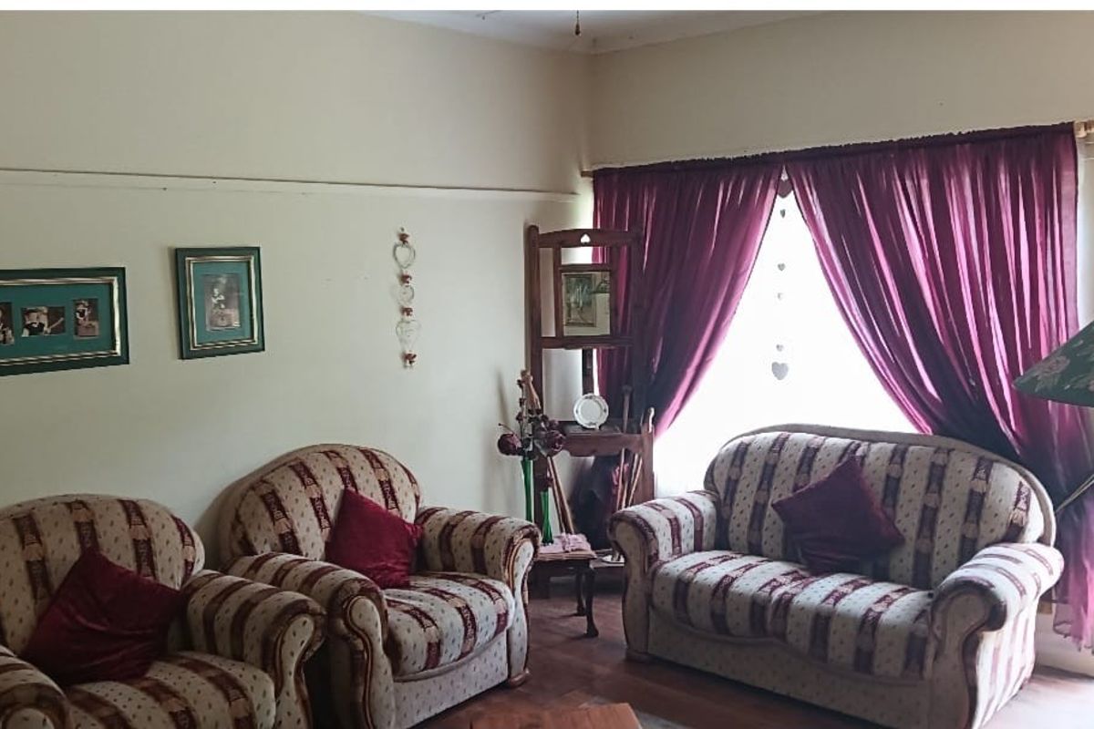 A living room featuring wooden flooring, a large window with curtains, and a door leading to an outdoor area.