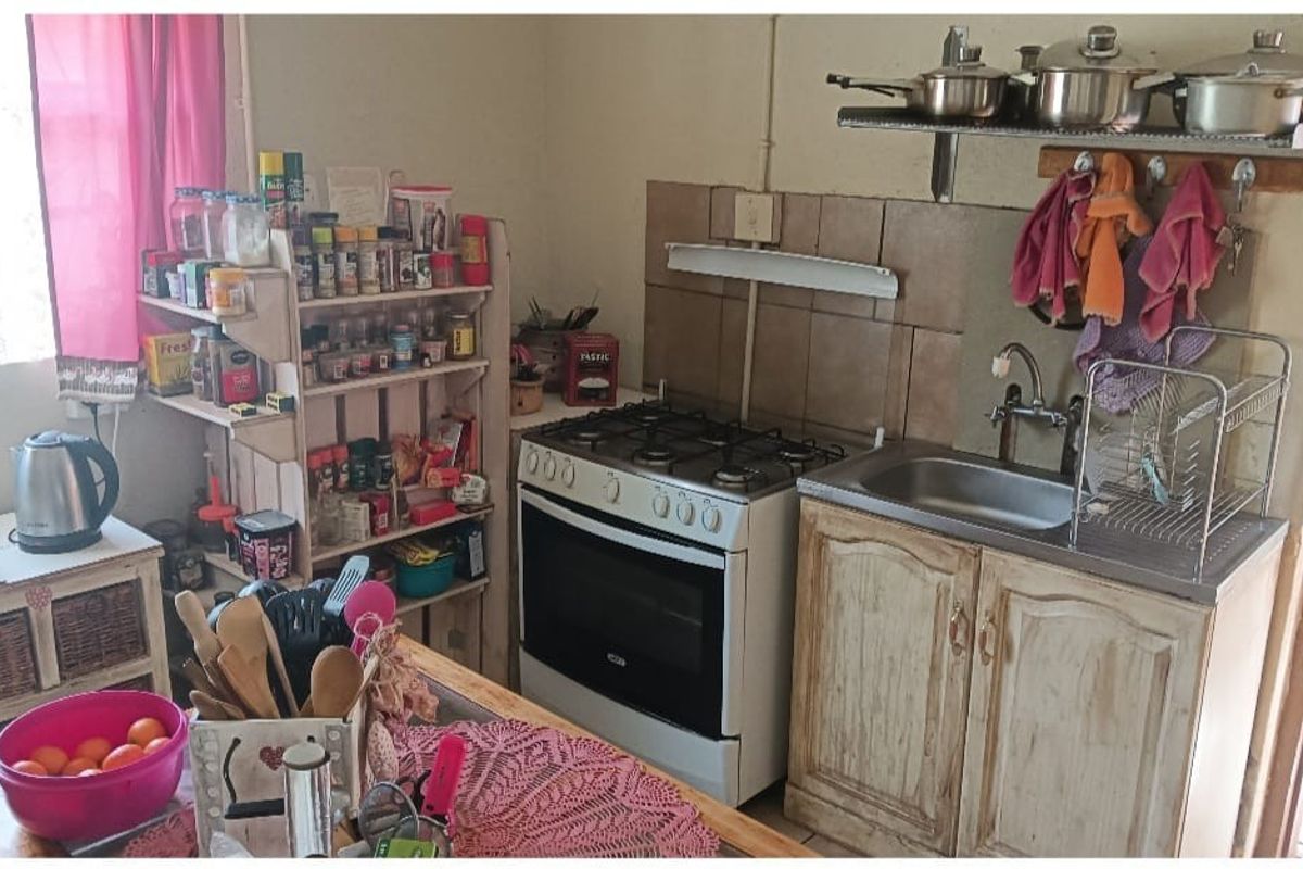 A compact kitchen featuring a gas stove, stainless steel sink, and wall-mounted shelving, offering a functional prep area with a rustic aesthetic.