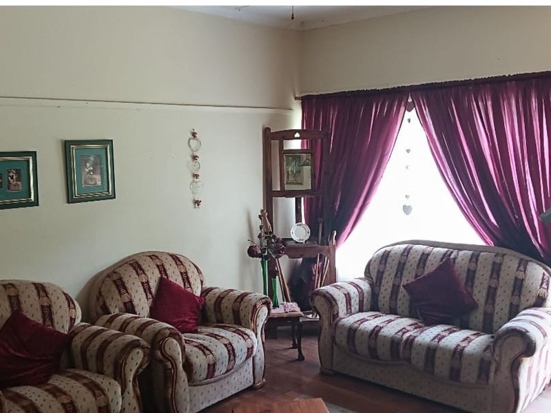 A living room featuring wooden flooring, a large window with curtains, and a door leading to an outdoor area.