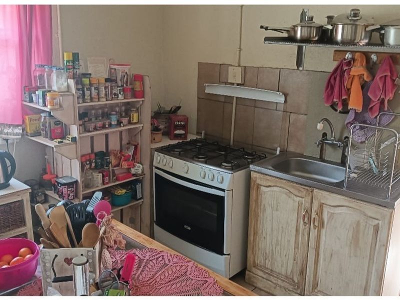 A compact kitchen featuring a gas stove, stainless steel sink, and wall-mounted shelving, offering a functional prep area with a rustic aesthetic.