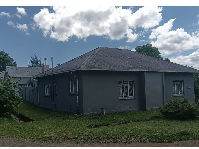 A detached single-story house featuring a dark grey exterior finish, a corrugated metal roof, and security bars on the windows.