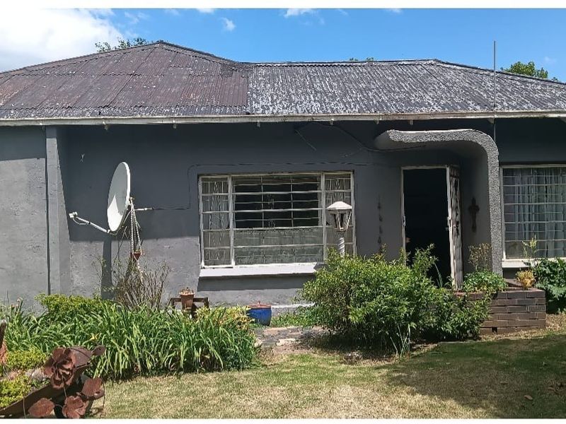 Front elevation of a single-story house featuring a corrugated metal roof, security bars on windows, and a small front garden area.