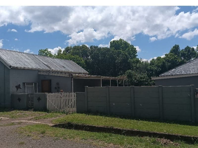 Exterior view of a detached house featuring a corrugated metal roof, perimeter boundary wall, and a gated entrance area.