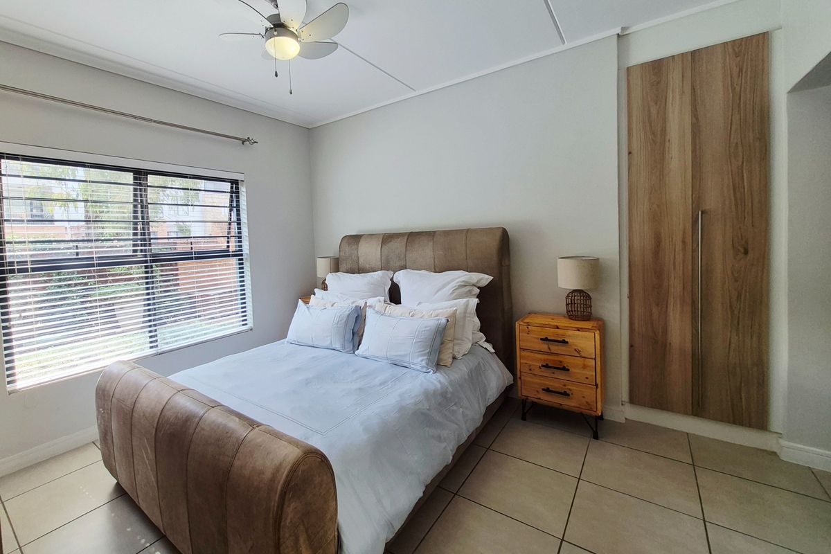 A well-maintained bedroom featuring neutral tiled flooring, a built-in wooden wardrobe, and a ceiling fan.