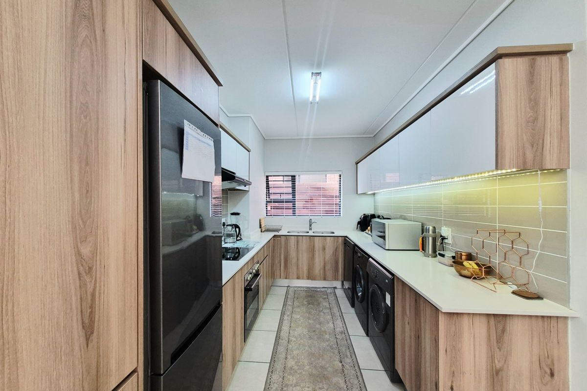 Modern galley-style kitchen featuring wood-grain cabinetry, white stone countertops, integrated appliances, and under-cabinet lighting.