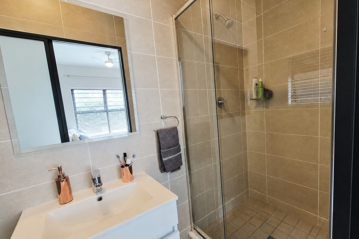 Modern bathroom featuring a sleek vanity with basin, a frameless glass shower enclosure, and neutral wall tiling.