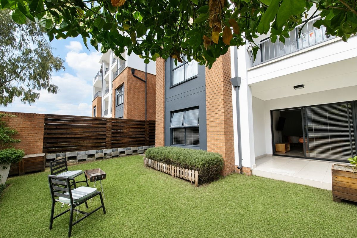 A private ground floor garden area featuring a paved patio, synthetic lawn, and brick boundary wall, adjacent to the townhouse living space.