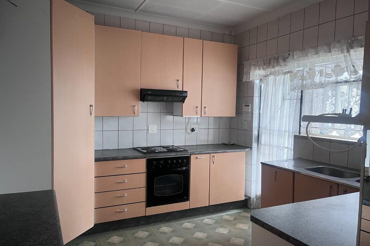 A dated kitchen featuring peach-toned cabinetry, a built-in oven and hob, extractor fan, and tiled splashbacks with a functional layout.