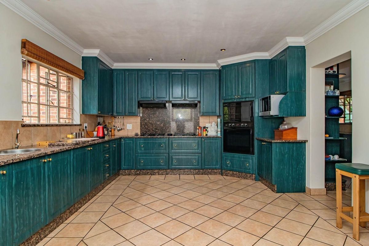 A spacious kitchen featuring teal-toned cabinetry, granite countertops, built-in oven, and tiled flooring with a classic layout.