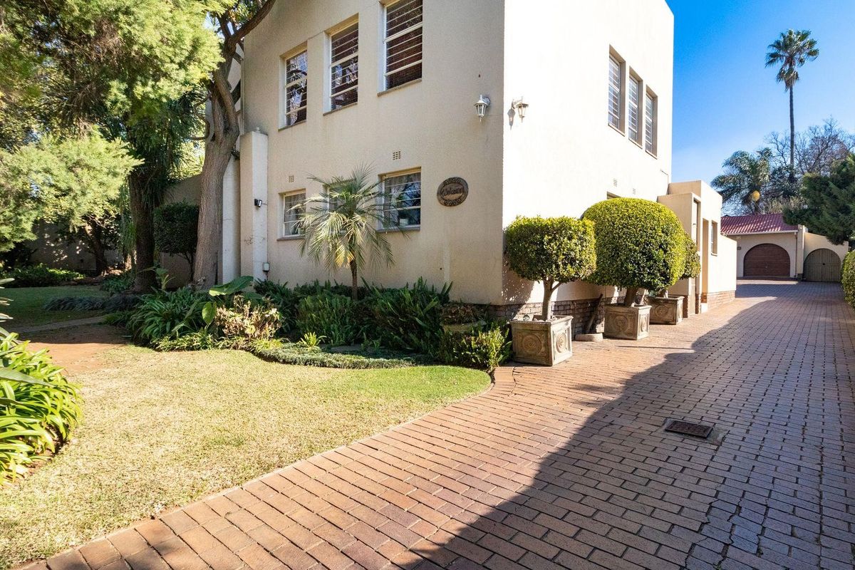 A view of the side elevation of the house featuring a paved driveway, landscaped garden, and established trees.