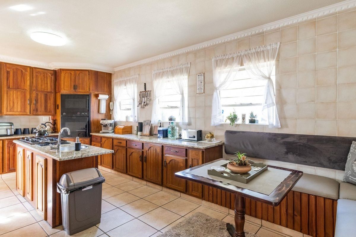 Spacious kitchen featuring timber cabinetry, granite countertops, a central island with a built-in hob, and integrated dining bench seating.