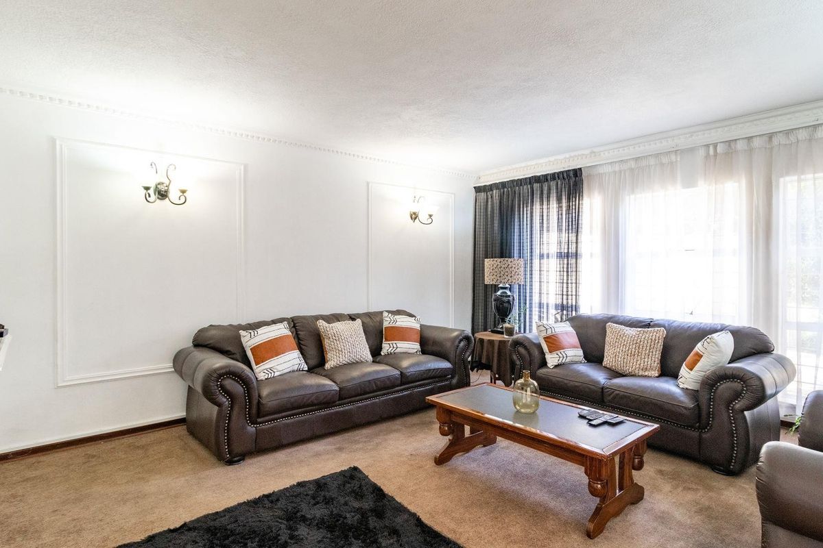 A spacious living room featuring wall molding, wall-mounted light fixtures, and large windows with curtains, providing a comfortable and well-lit living space.