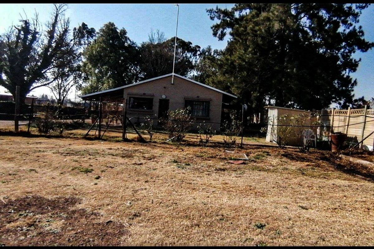 Rear view of the property featuring a covered patio, security bars on windows, and a large garden area with an outbuilding.
