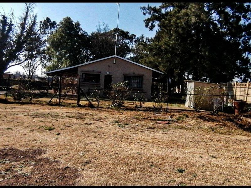 Rear view of the property featuring a covered patio, security bars on windows, and a large garden area with an outbuilding.