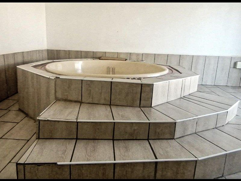 A dated bathroom featuring a built-in circular bathtub elevated on a tiled platform with steps.