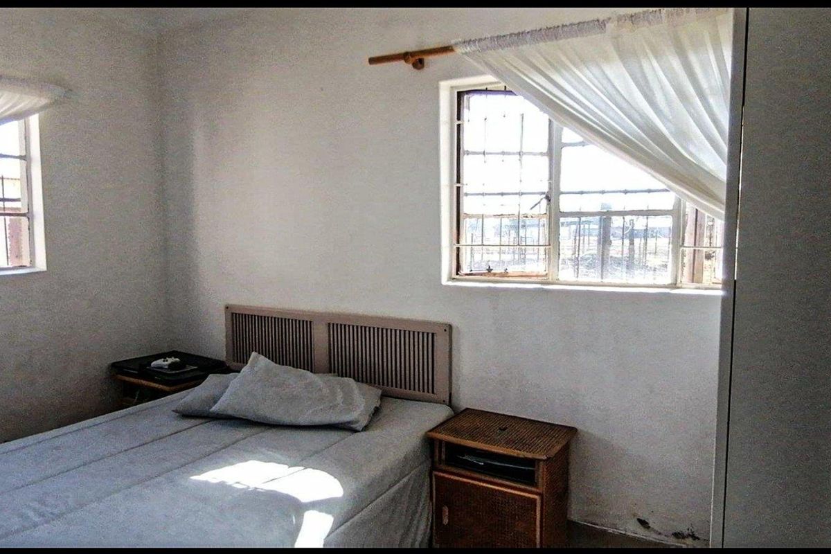 A compact bedroom featuring security bars on the windows and basic finishes, requiring some cosmetic updates to improve its overall appeal.