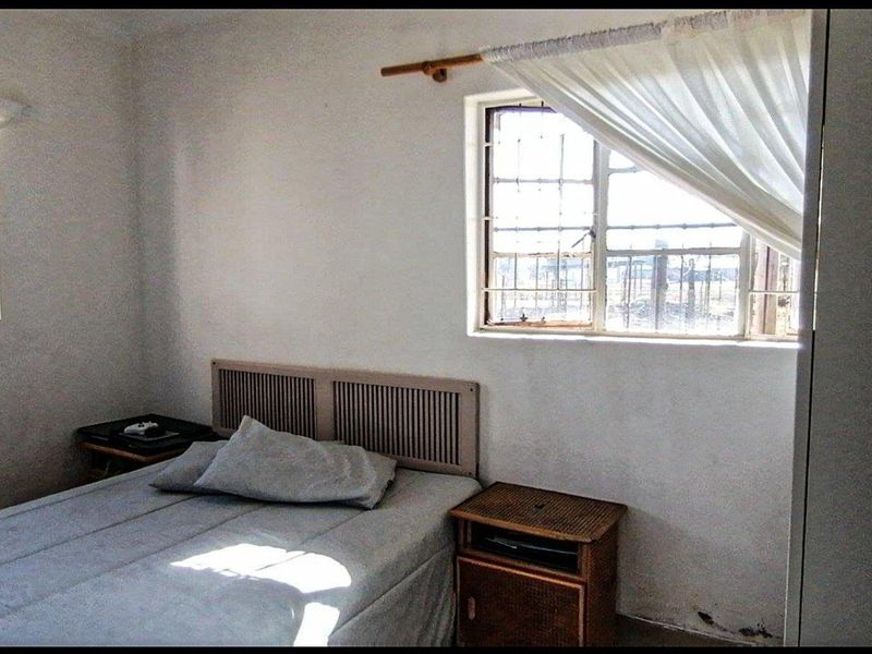 A compact bedroom featuring security bars on the windows and basic finishes, requiring some cosmetic updates to improve its overall appeal.