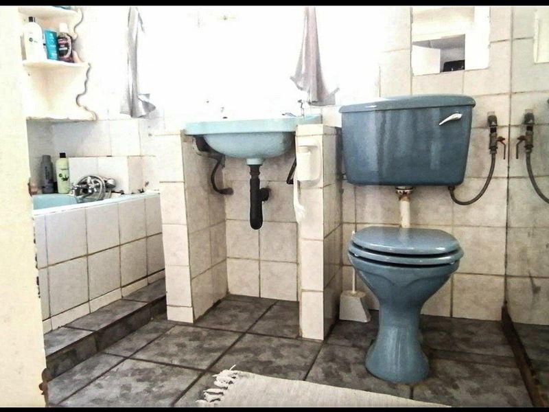 A dated bathroom featuring blue sanitaryware, tiled walls and flooring, and a built-in vanity, offering significant potential for a modern renovation.