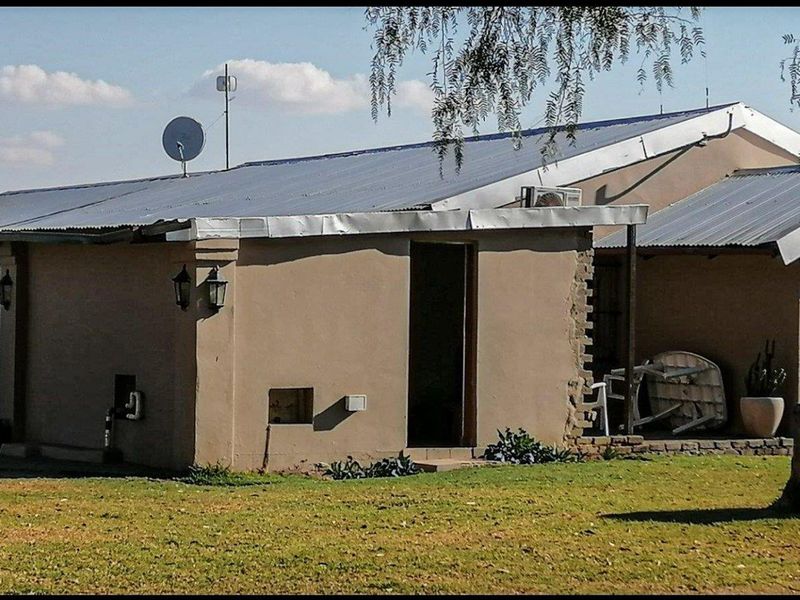 Rear view of a single-story house featuring a corrugated metal roof, security bars on windows, and an exterior air conditioning unit.