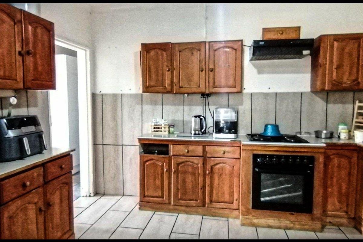 A dated kitchen featuring wooden cabinetry, a built-in oven with gas hob, extractor fan, and tiled backsplash, requiring cosmetic updates to modernize the space.