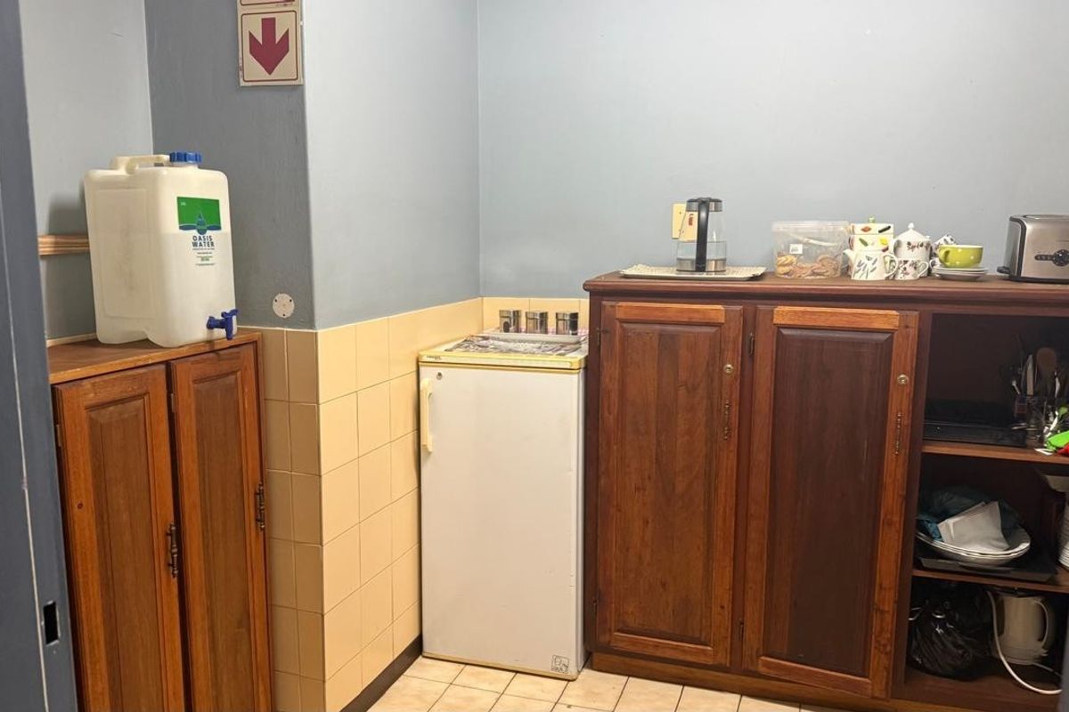 A functional kitchenette area featuring built-in wooden cabinetry, tiled splashbacks, and tiled flooring, suitable for office or industrial utility use.