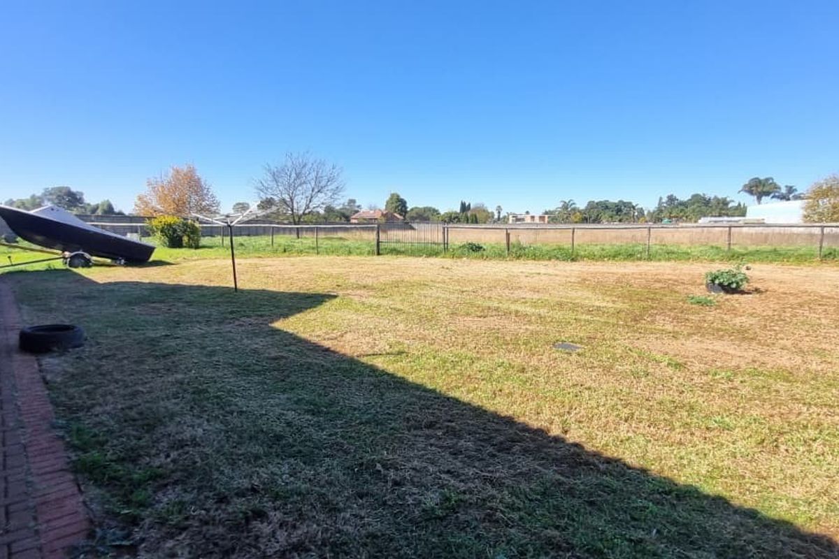 A spacious rear garden area featuring a brick-paved walkway along the side of the house and perimeter fencing.