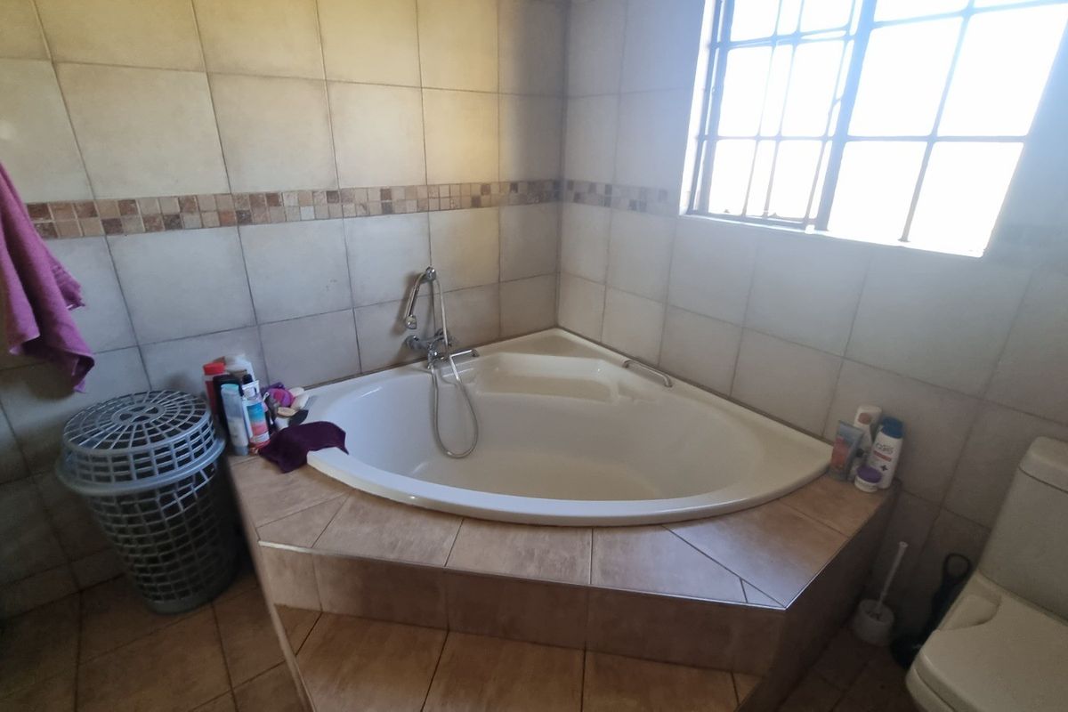 A functional bathroom featuring a built-in corner bathtub with tiled surround and a standard toilet.