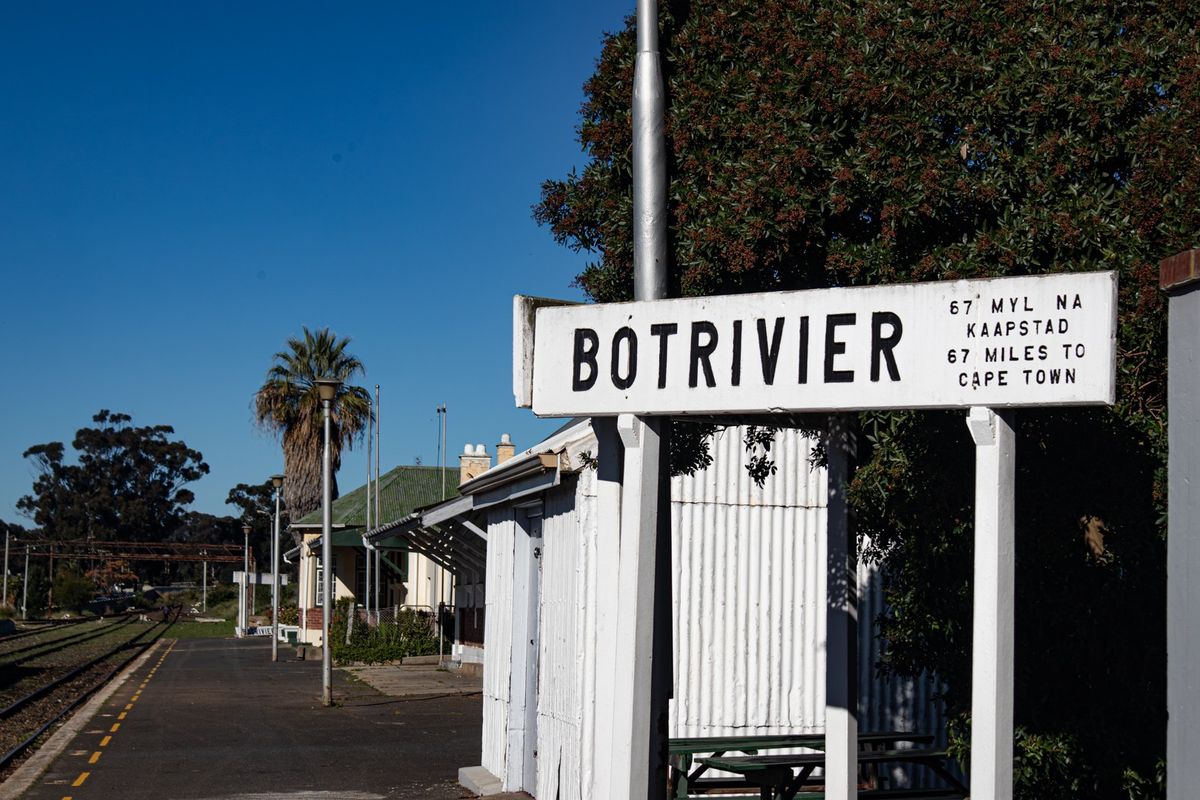 A view of the Botrivier railway station platform and signage, highlighting the local transport infrastructure and surrounding landscape.