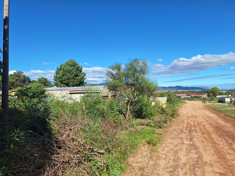 A view of a vacant residential plot featuring unpaved road access and surrounding natural vegetation with distant mountain views.