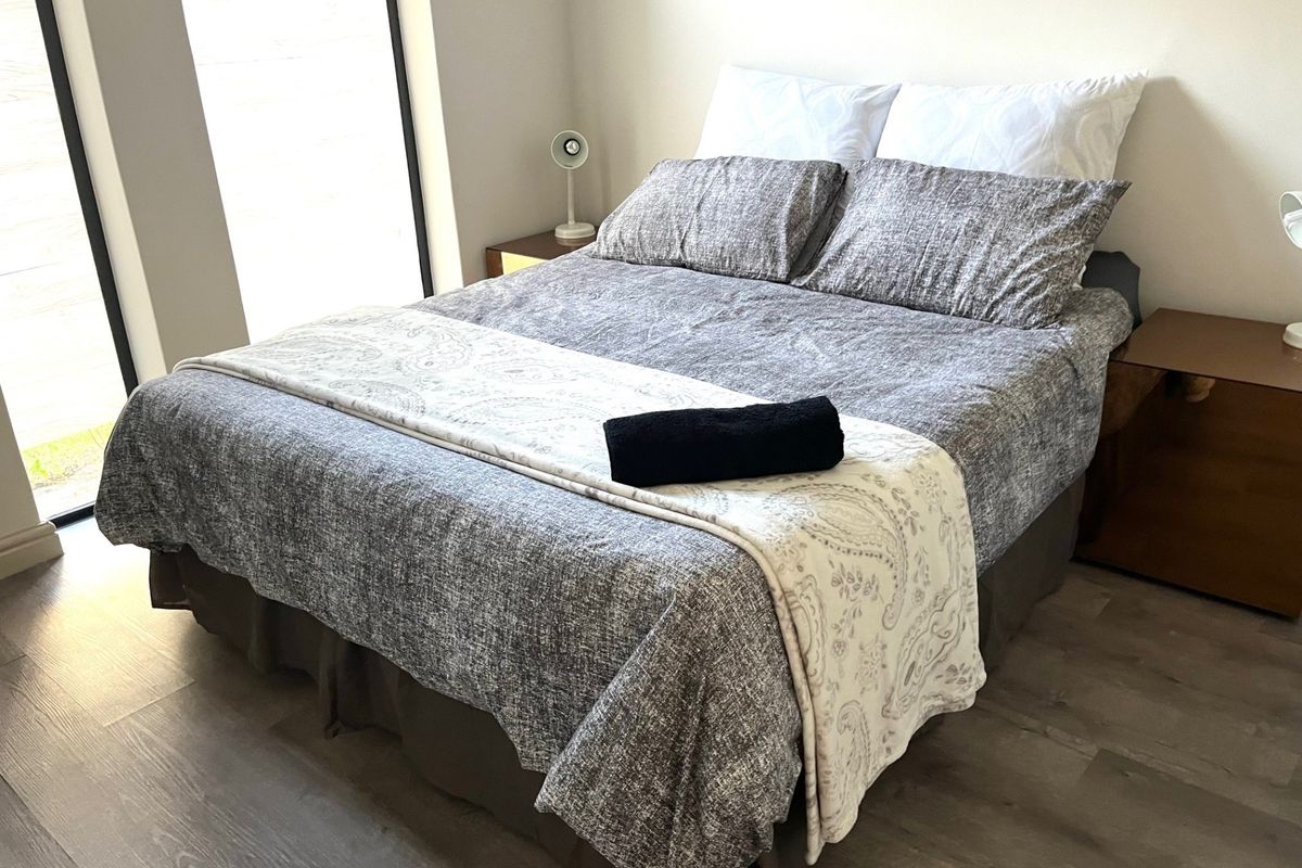 A well-maintained bedroom featuring modern laminate flooring and a large window providing natural light.