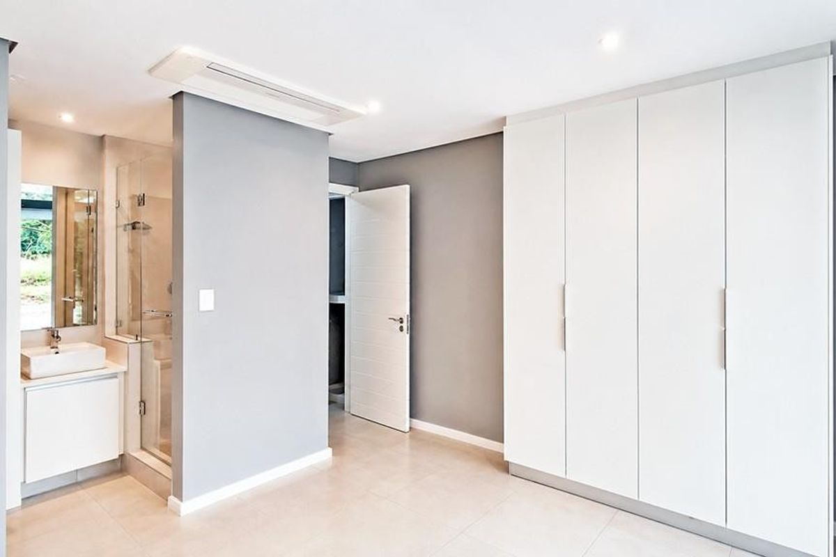 Modern bedroom featuring built-in floor-to-ceiling wardrobes, recessed ceiling lighting, and an integrated en-suite bathroom with a glass-enclosed shower and vanity.