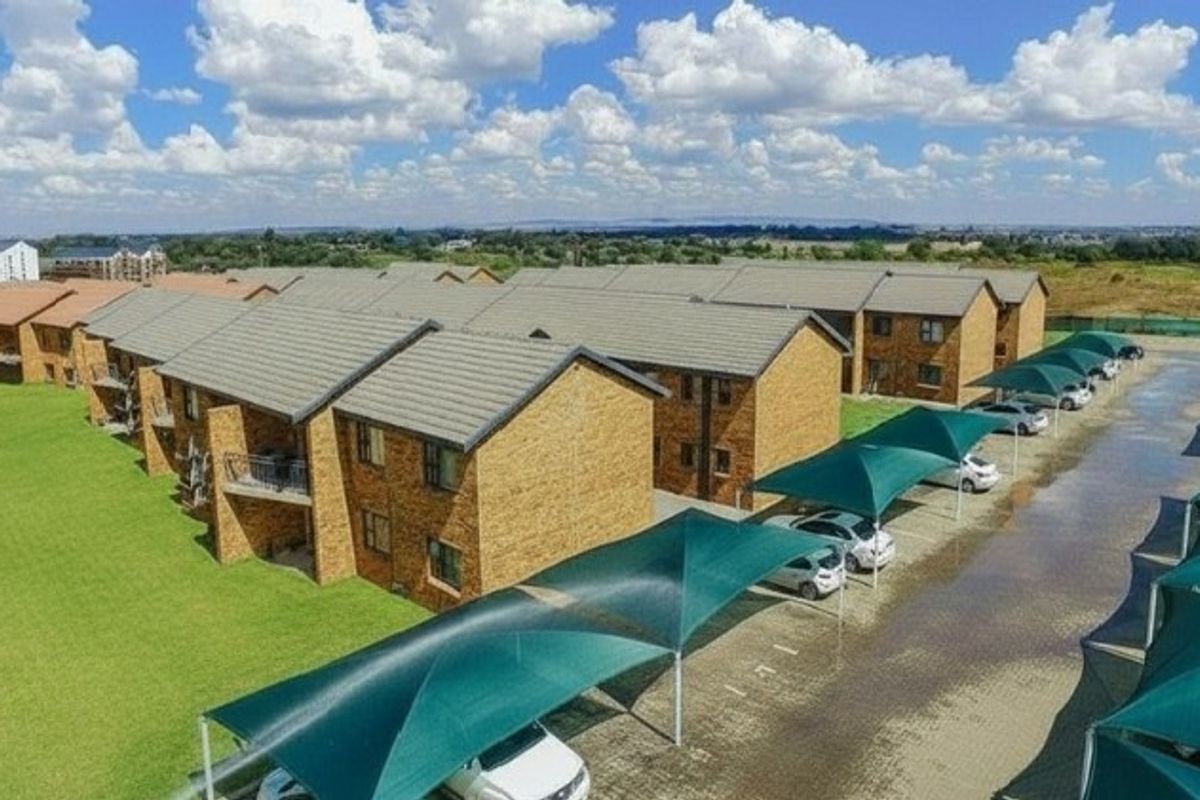 Aerial view of a residential apartment complex featuring brick buildings, tiled roofs, and designated shaded parking bays.
