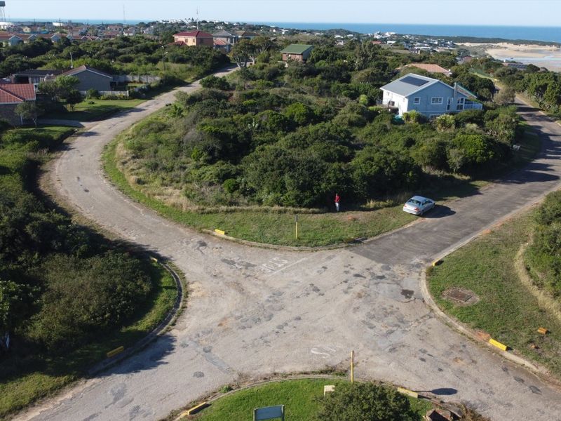 An aerial view of a vacant residential plot situated in a coastal neighborhood, featuring natural vegetation and proximity to local road infrastructure.