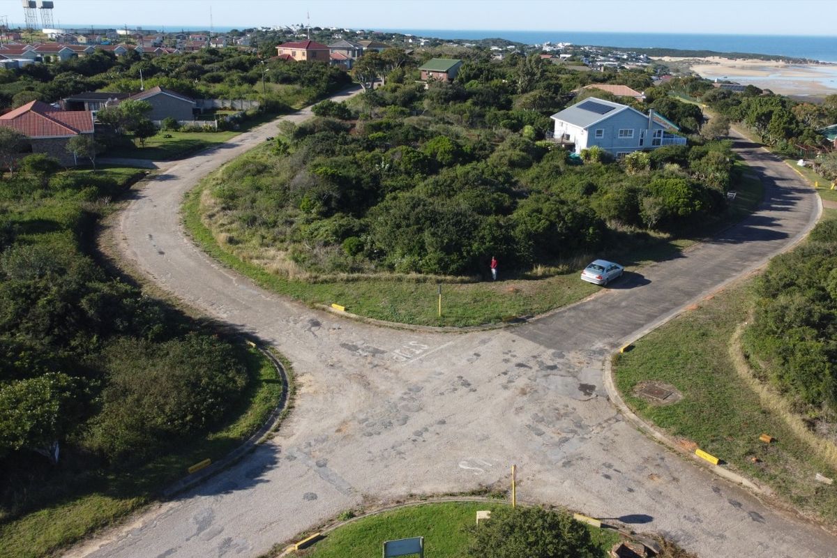 An aerial view of a vacant residential plot situated in a coastal neighborhood, featuring natural vegetation and proximity to local road infrastructure.