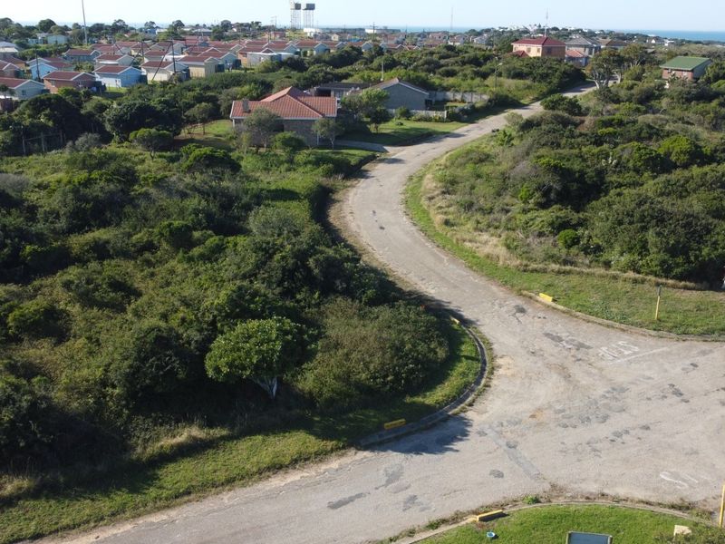 An aerial view of a vacant residential plot featuring natural vegetation and access to an existing local road network in a coastal neighborhood.