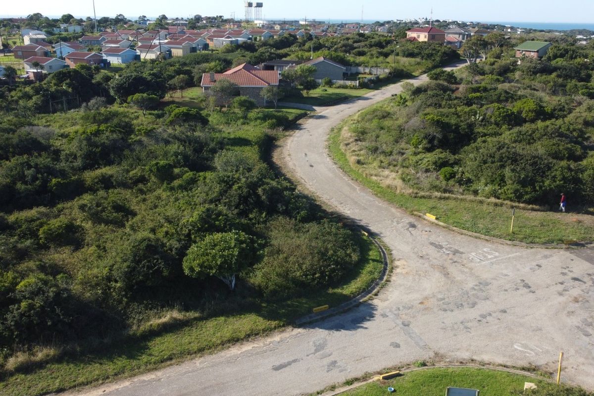 An aerial view of a vacant residential plot featuring natural vegetation and access to an existing local road network in a coastal neighborhood.
