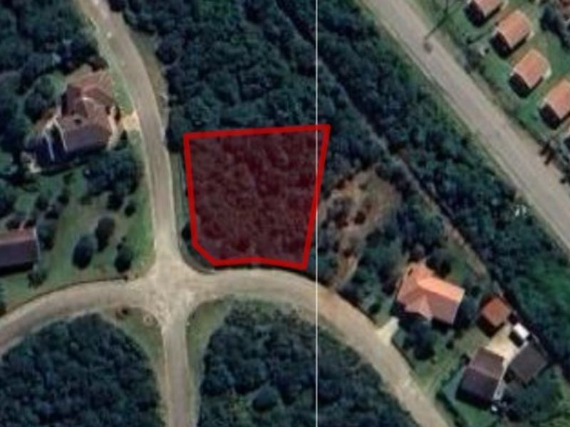 An aerial view of a vacant residential plot highlighted in red, situated within a developed neighborhood with established road access.