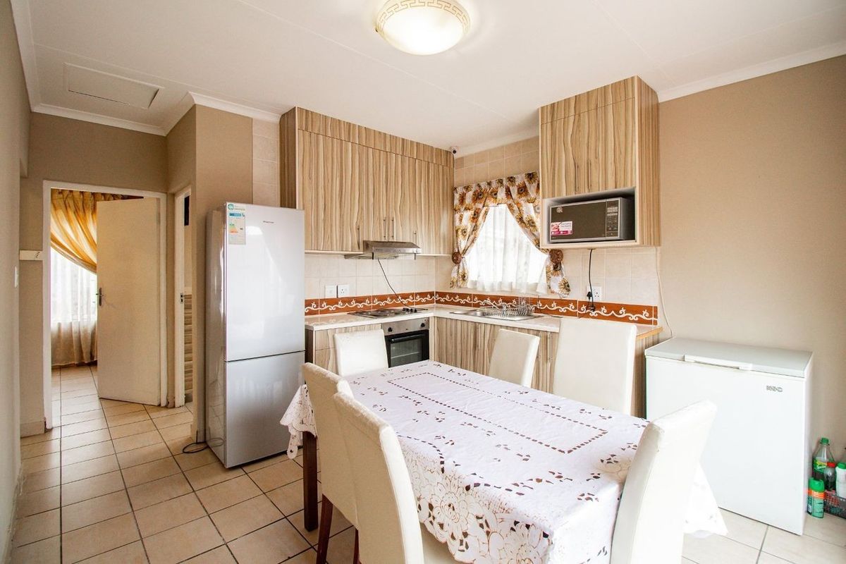 A functional kitchen featuring wood-look cabinetry, tiled flooring, a built-in oven, hob, and extractor fan, with an adjacent dining area.