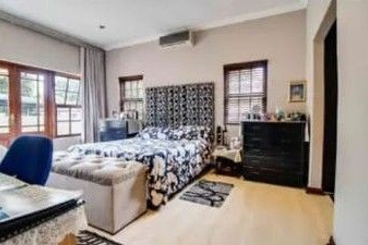 A spacious bedroom featuring timber-framed windows, a wall-mounted air conditioning unit, and light-toned flooring.