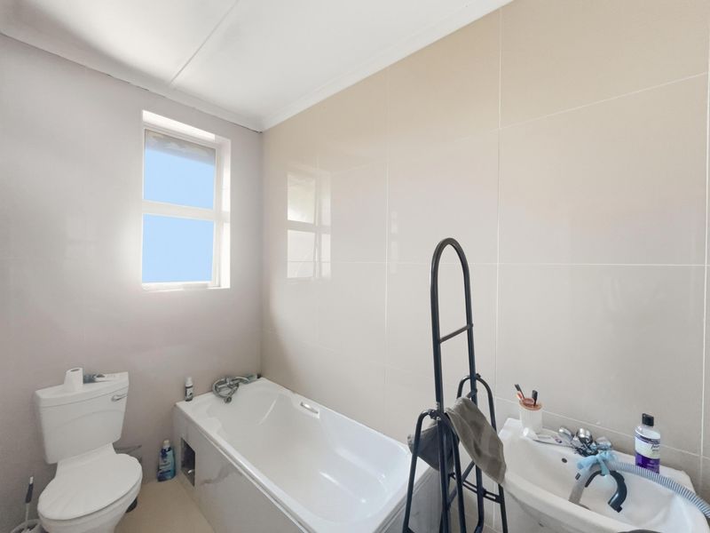 A functional bathroom featuring a bathtub, pedestal basin, and toilet with neutral wall tiling and natural light from a side window.